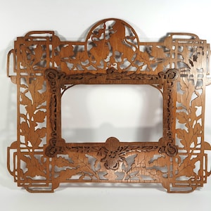 May include: Ornate wooden picture frame with intricate cut-out designs. The frame features a rectangular opening, surrounded by detailed carvings of leaves, floral patterns, and mythical creatures. The frame is a warm brown color and is suitable for home decor.