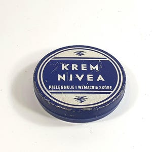 Op de afbeelding: Vintage Nivea crèmeblikje, blauw en wit. Het ronde blikje toont de merknaam in witte letters op een blauwe achtergrond, met Poolse tekst. Een klassieke verpakking voor huidverzorgingsproducten.