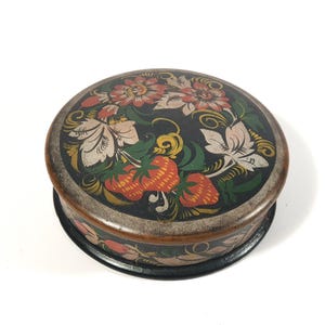 May include: A round wooden box with a black background and a floral design painted in red, orange, yellow, green, and white. The flowers are stylized and resemble strawberries.