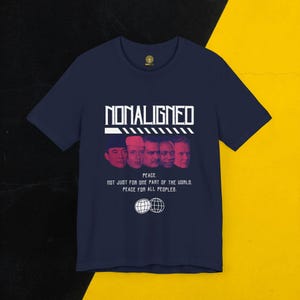 Könnte beinhalten: Marineblaues T-Shirt mit dem Wort "NONALIGNED" in Weiß über fünf Gesichtern. Darunter steht der Text "PEACE. NOT JUST FOR ONE PART OF THE WORLD. PEACE FOR ALL PEOPLES."