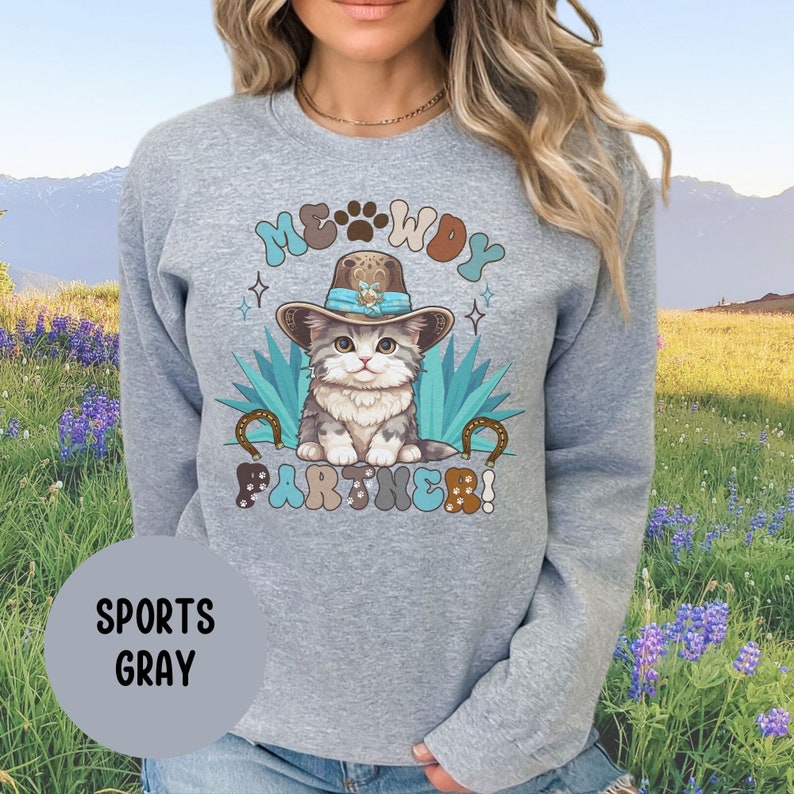 May include: A gray sweatshirt with a cartoon cat wearing a cowboy hat and the text "MEOWDY PARTNER!" printed on the front. The cat is sitting on a cactus with a horseshoe on each side. The sweatshirt is a sports gray color.