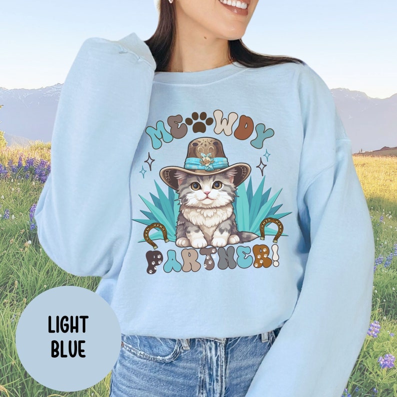 May include: Light blue sweatshirt with a cartoon cat wearing a cowboy hat and the text "MEOWDY PARTNER!" printed on the front.
