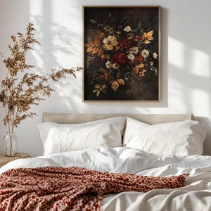 K&ouml;nnte beinhalten: Gerahmter Blumendruck mit dunklem Hintergrund, der einen Strau&szlig; roter, wei&szlig;er und gelber Blumen und Herbstbl&auml;tter zeigt. Das Kunstwerk h&auml;ngt &uuml;ber einem Bett mit wei&szlig;er Bettw&auml;sche und einer rot gemusterten Decke.