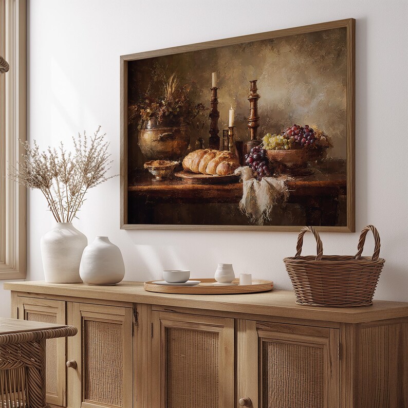 May include: A framed still life painting depicts a table laden with food and objects. A loaf of bread, grapes, and a bowl of nuts are on the table. Two candlesticks with lit candles and a vase of flowers are also present.