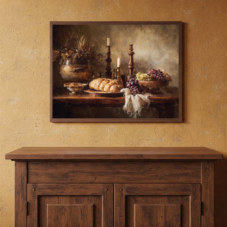 May include: A framed still life painting depicts a rustic table laden with food. A loaf of bread, grapes, and a bowl of fruit are arranged with candles and a decorative vase. The color palette is warm, with browns, golds, and hints of purple.