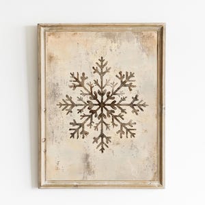 Puede incluir: Una impresión enmarcada de un copo de nieve marrón sobre un fondo beige. El marco es de madera clara con un acabado desgastado.