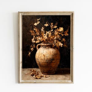 Puede incluir: Pintura de naturaleza muerta vintage enmarcada, que presenta un jarrón grande de terracota envejecida lleno de hojas y ramas doradas secas. El jarrón se encuentra sobre una superficie neutra contra un fondo oscuro, con hojas caídas.