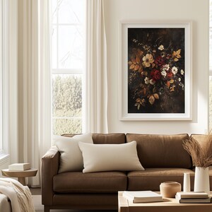 K&ouml;nnte beinhalten: Ein gerahmter Kunstdruck mit Blumenmotiv, der einen dunklen Hintergrund und einen Strau&szlig; roter, wei&szlig;er und gelber Blumen zeigt. Das Kunstwerk h&auml;ngt &uuml;ber einem braunen Ledersofa mit cremefarbenen Kissen. Ein Holztisch und eine wei&szlig;e Vase mit getrockneten Pflanzen sind ebenfalls zu sehen.
