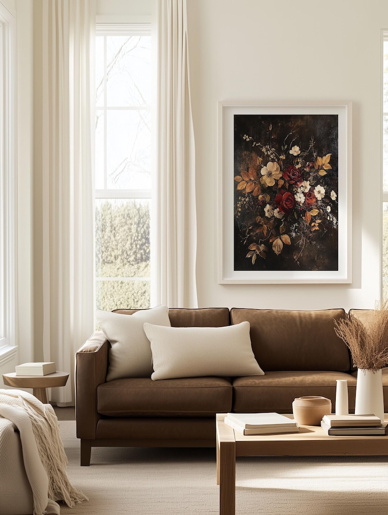 K&ouml;nnte beinhalten: Ein gerahmter Kunstdruck mit Blumenmotiv, der einen dunklen Hintergrund und einen Strau&szlig; roter, wei&szlig;er und gelber Blumen zeigt. Das Kunstwerk h&auml;ngt &uuml;ber einem braunen Ledersofa mit cremefarbenen Kissen. Ein Holztisch und eine wei&szlig;e Vase mit getrockneten Pflanzen sind ebenfalls zu sehen.