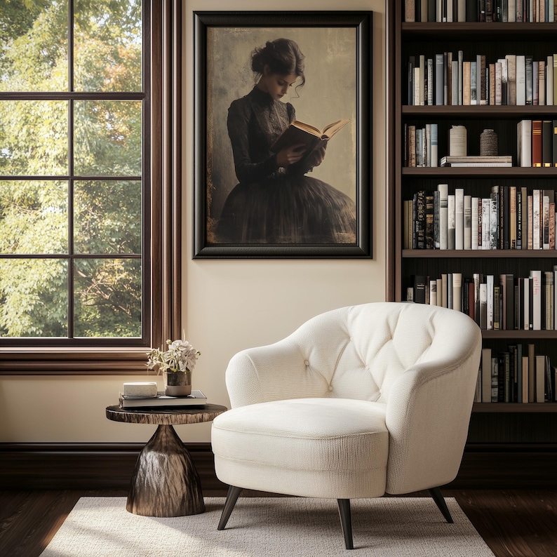 May include: A white tufted armchair with a wooden frame and black legs sits in a room with a window, a bookshelf, and a side table with a vase of flowers. A framed picture of a woman reading a book hangs on the wall.