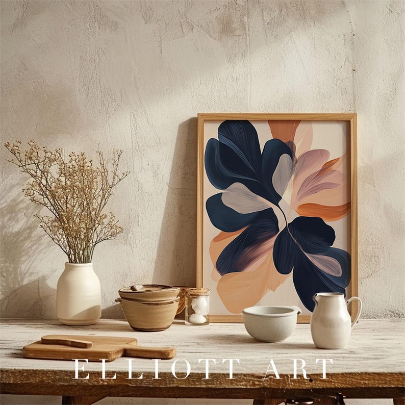 May include: A framed art print featuring an abstract floral design in navy, peach, and blush tones. The artwork is displayed on a wooden table alongside a vase, bowls, and a pitcher. The text "ELLIOTT ART" is at the bottom.