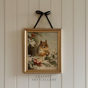 May include: A framed print of a squirrel holding a pine cone in a snowy winter scene. The print is in a gold-colored frame and is suspended by a black ribbon. The text "ELLIOTT ART GALLERY" is at the bottom of the frame.