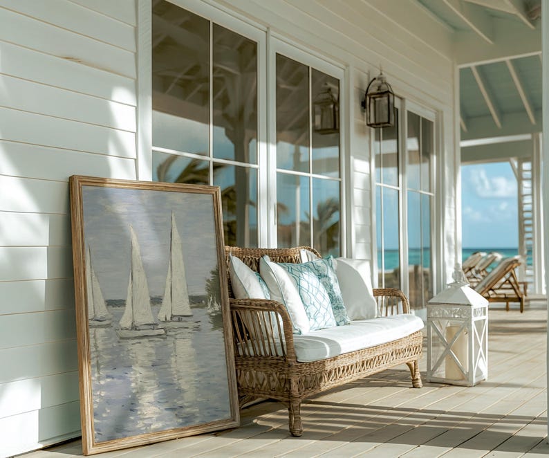 May include: A coastal scene featuring a framed sailboat painting, a wicker loveseat with white and blue pillows, and a white lantern. The setting is a porch with large windows and a view of the ocean.