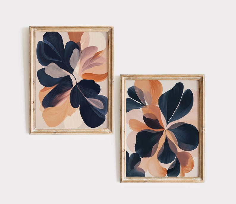 May include: Two framed abstract art prints. Each print features a floral design with navy blue, peach, and blush-colored brushstrokes. The frames are a light wood color, and the art is displayed against a white background.