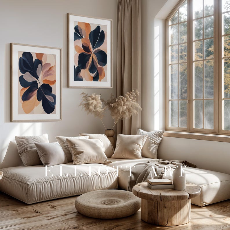 May include: Two framed abstract art prints with botanical designs in navy, peach, and beige tones hang above a beige sectional sofa. The room features a wooden coffee table, a round ottoman, and a large window with natural light.