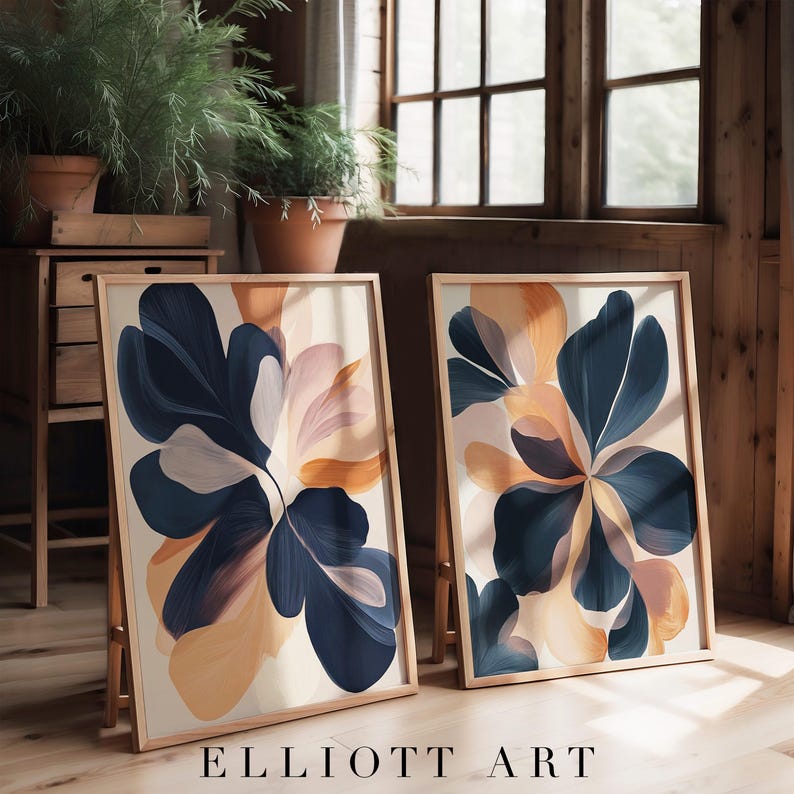 May include: Two framed abstract floral art prints. Each print features a large, stylized flower in shades of navy blue, peach, and cream against a neutral background. The prints are displayed on wooden easels, with the text "ELLIOTT ART" at the bottom.