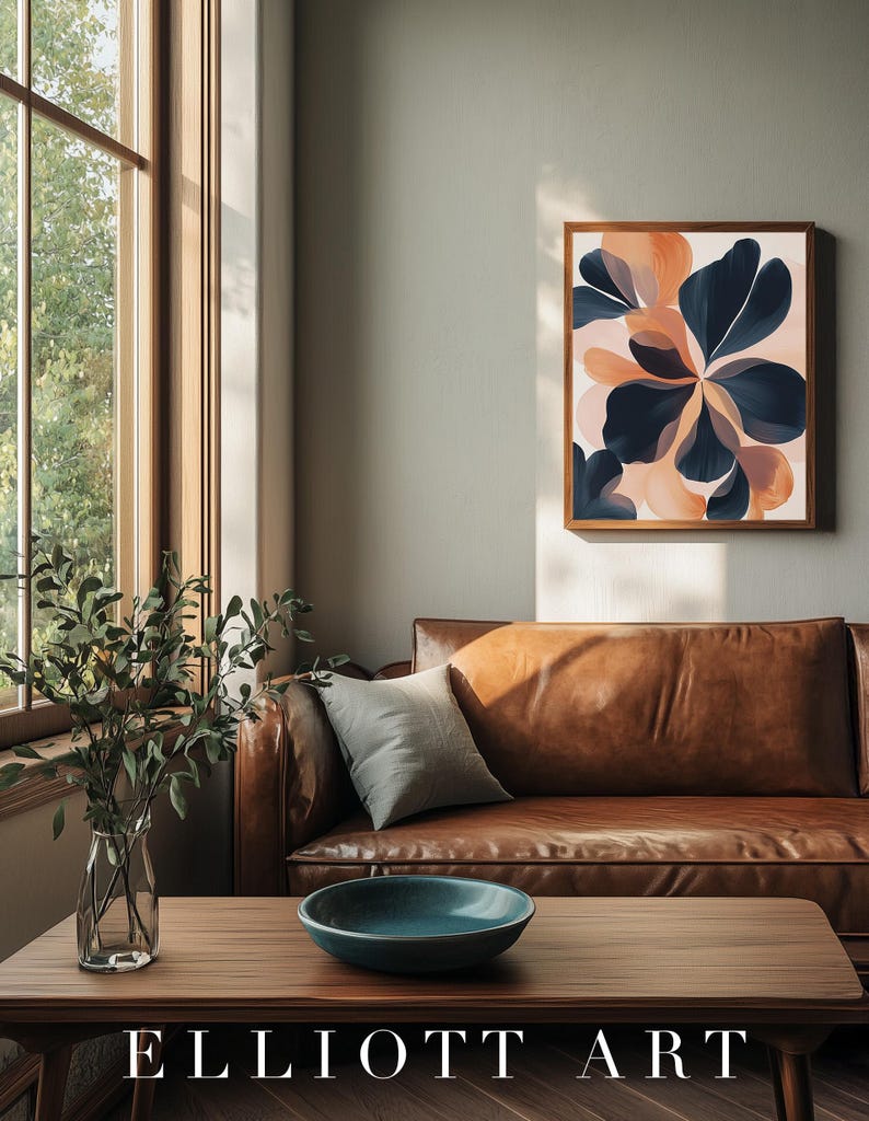 May include: A framed abstract floral art print with navy blue and peach-colored petal shapes. The artwork hangs above a brown leather sofa. A wooden coffee table with a teal bowl and a vase of greenery is in front of the sofa. The text "ELLIOTT ART" is at the bottom.