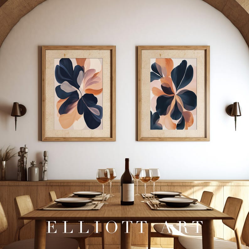 May include: Two framed abstract floral art prints. Each print features navy blue, peach, and cream-colored botanical shapes. The prints are displayed above a wooden dining table set for a meal, with wine glasses and a bottle of wine.