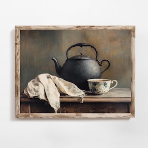 Puede incluir: Pintura enmarcada de naturaleza muerta con una tetera gris oscuro, una taza de té blanca y azul y un paño color crema. La pintura está sobre una mesa de madera con un fondo neutro. La obra está enmarcada en un marco de madera marrón claro.