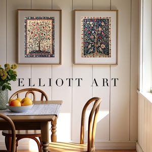 May include: Two framed art prints with tree and bird designs hang on a white wall. The prints are in gold frames. A wooden table with a vase of flowers and a bowl of fruit sits below the art. The text "ELLIOTT ART" is below the art prints.