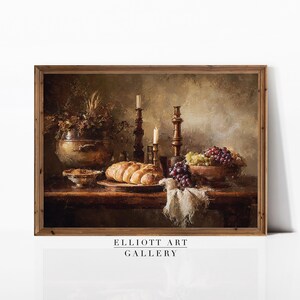 May include: A framed still life painting featuring a rustic table setting. The scene includes a loaf of bread, grapes, candles, and a decorative bowl. The color palette is dominated by warm browns and golds, creating a vintage aesthetic. The text "ELLIOTT ART GALLERY" is at the bottom.