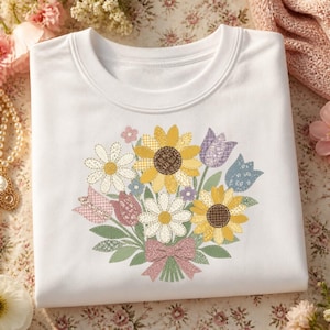 Peut inclure: Un t-shirt blanc à col rond orné d'un motif central représentant un bouquet de fleurs. Le dessin comprend des tournesols, des marguerites et des tulipes dans des tons jaunes, roses, bleus et blancs, avec un nœud rose et des feuilles vertes.