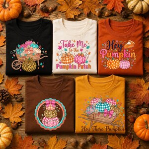 Peut inclure: Cinq t-shirts avec des motifs sur le thème de l'automne. Un t-shirt noir avec une brouette de citrouilles, un crème avec le texte Take Me to the Pumpkin Patch, un orange avec Hey Pumpkin, un marron avec des citrouilles empilées et un jaune.