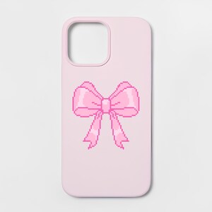May include: A light pink phone case featuring a centered pixel art graphic of a bow. The bow is rendered in various shades of pink, including a darker magenta outline and lighter pink highlights, creating a distinct blocky, digital aesthetic.