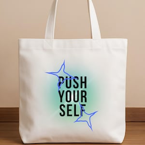 May include: A white canvas tote bag featuring the black text PUSH YOUR SELF centered on the front. The text is surrounded by a soft, glowing mint green circular aura and two blue four-pointed star shapes positioned at the top left and bottom right.