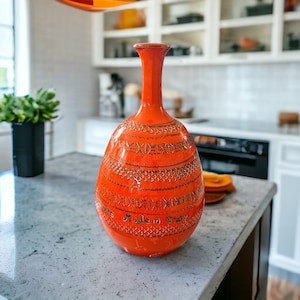 May include: A vibrant orange ceramic vase with a slender neck and rounded body. The vase has a textured design and the words "Made in Italy". It is displayed on a countertop.