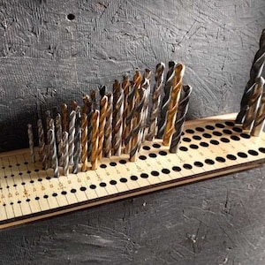 May include: A wooden drill bit organiser with a variety of drill bits in different sizes and colours. The organiser has a grid of holes to hold the drill bits in place. The drill bits are arranged in a curved pattern.