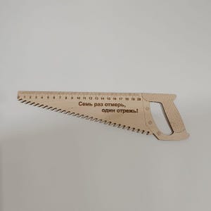 Op de afbeelding: Een houten zaagliniaal met een handvat en een meetschaal van 50 cm. Op de liniaal staat de tekst "Семь раз отмерь, один отрежь!" gegraveerd.