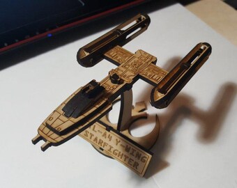 May include: A wooden model of a Star Wars L-A4 Y-wing Starfighter on a stand. The model is detailed and has a brown wood finish. The stand has the words "L-A4 Y-wing Starfighter" engraved on it.