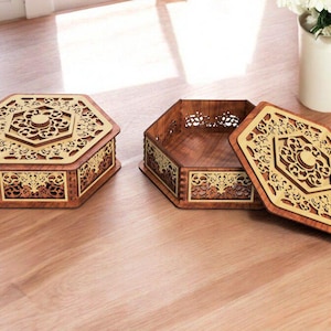 May include: Two hexagonal wooden boxes with intricate laser cut designs. The boxes are made of dark wood with a light gold inlay. The lid of one box is open, revealing the interior.
