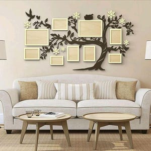 May include: A white sofa with cushions sits in front of a wall with a decorative wooden tree design. The tree is made of branches and leaves with multiple picture frames attached to it. The frames are all empty.