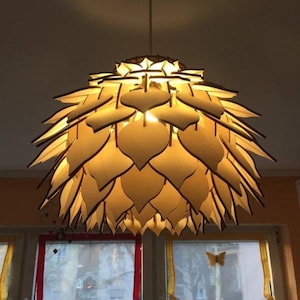 Op de afbeelding: Een houten hanglamp met een uniek ontwerp dat lijkt op een bloem. De lamp is gemaakt van veel afzonderlijke stukken hout die in bladvormen zijn gesneden en samengevoegd om een ​​bolvorm te creëren. De lamp wordt van binnenuit verlicht en geeft een warm licht.