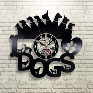 Może przedstawiać: Czarny zegar winylowy z wzorem odcisku łapy i napisem "DOGS" dużymi literami. Tarcza zegara ma srebrne tło z czarnymi cyframi i wskazówkami.