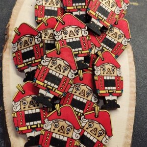 Peut inclure: Une collection d'ornements de casse-noisette en bois avec des chapeaux rouges et des visages blancs. Les casse-noisettes sont peints avec des détails dorés et noirs et ont un aspect fantaisiste et festif.
