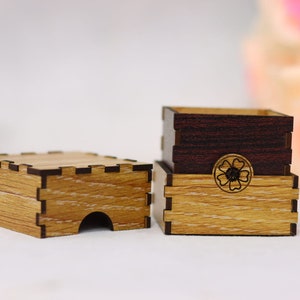 May include: Two wooden boxes with a decorative flower design. The top box is dark brown wood and the bottom box is light brown wood.