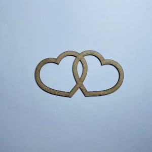 Puede incluir: Dos corazones de madera entrelazados, creando un símbolo de amor y unidad. Los corazones están cortados de madera marrón claro y se colocan sobre un fondo blanco.