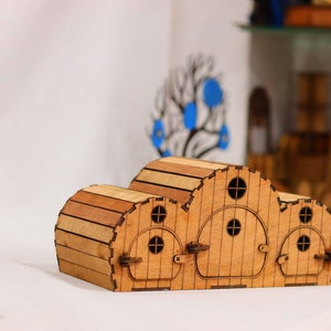 Puede incluir: Un modelo de madera de una casa con tres puertas y ventanas redondeadas. La casa está hecha de madera marrón claro y tiene un aspecto rústico.