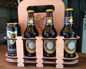 May include: Wooden six-pack carrier with a brown stain finish. The carrier has a handle and holds three bottles of Coopers Best Extra Stout and one can of Guinness Draught.