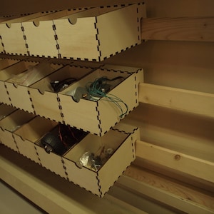 Könnte beinhalten: Ein Satz Holzschubladen mit hellbrauner Oberfläche. Die Schubladen sind übereinander gestapelt und offen, um verschiedene Kleinteile zu zeigen.