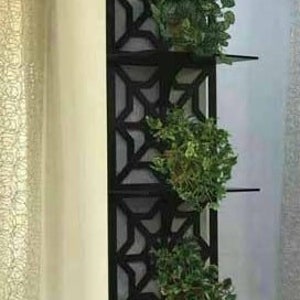 May include: A black metal wall shelf with a geometric design. The shelf has four tiers and is decorated with green plants.