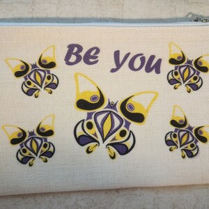 May include: A white canvas zippered pouch with a purple "Be You" message and a repeating pattern of yellow, purple, and black stylized butterflies.