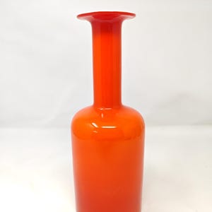 May include: A tall, orange glass vase with a flared top. The vase has a cylindrical body and a long, slender neck. The color is a vibrant, solid orange, with a glossy finish. The vase is likely used for decorative purposes.