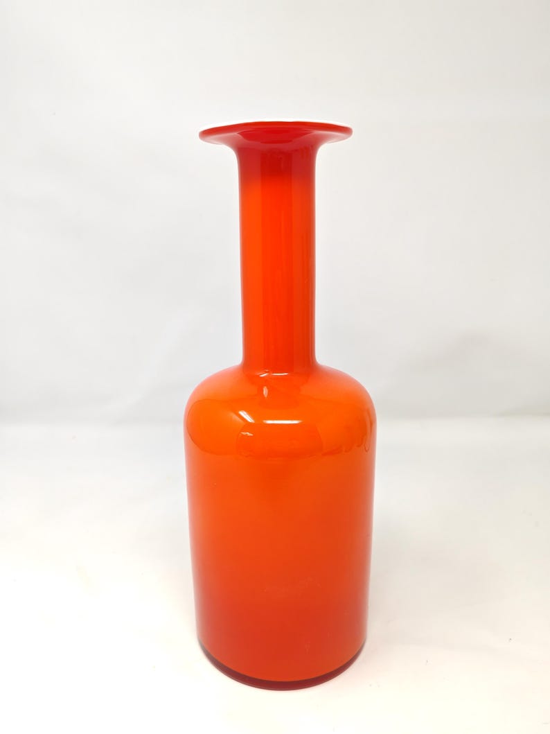 May include: A tall, orange glass vase with a flared top. The vase has a cylindrical body and a long, slender neck. The color is a vibrant, solid orange, with a glossy finish. The vase is likely used for decorative purposes.