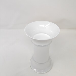 May include: A white, elegant vase with a flared top and a cylindrical body. The vase has a wide, circular base and a slightly narrower midsection. The overall design is simple and modern, suitable for various floral arrangements.