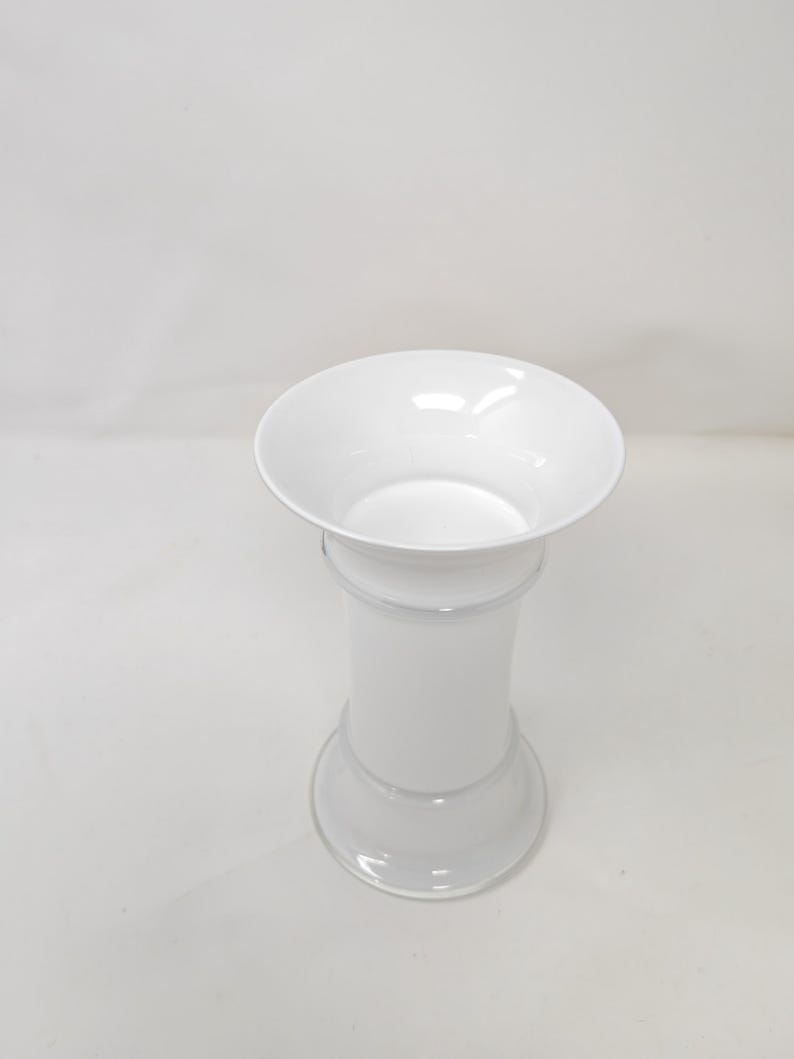 May include: A white, elegant vase with a flared top and a cylindrical body. The vase has a wide, circular base and a slightly narrower midsection. The overall design is simple and modern, suitable for various floral arrangements.