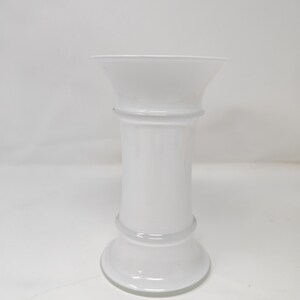 May include: A white, opaque glass vase with a flared top and a rounded base. The vase has a cylindrical body with two horizontal bands. The overall design is simple and elegant.